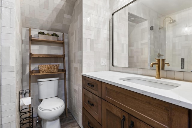 bathroom with vanity, toilet, tile walls, and a tile shower