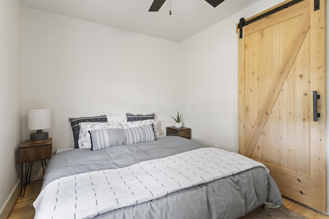 bedroom with wood-type flooring, a barn door, and ceiling fan