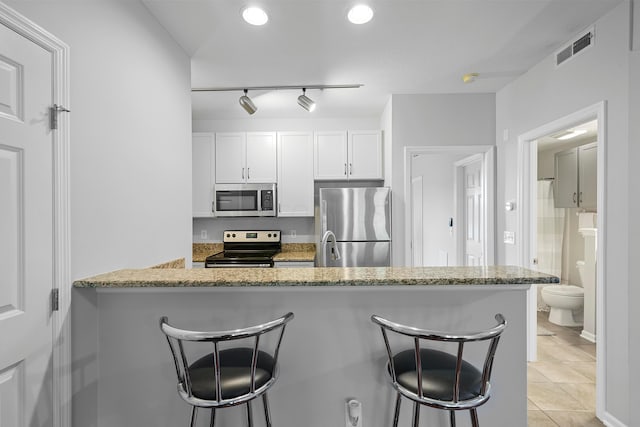 kitchen with light stone countertops, appliances with stainless steel finishes, a kitchen bar, kitchen peninsula, and white cabinetry