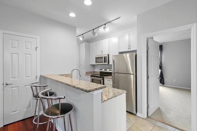 kitchen featuring light stone countertops, kitchen peninsula, a breakfast bar, stainless steel appliances, and white cabinetry