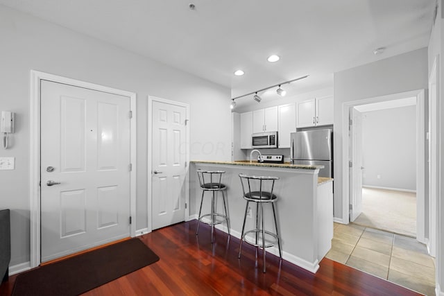 kitchen featuring a kitchen breakfast bar, kitchen peninsula, light hardwood / wood-style flooring, white cabinetry, and stainless steel appliances