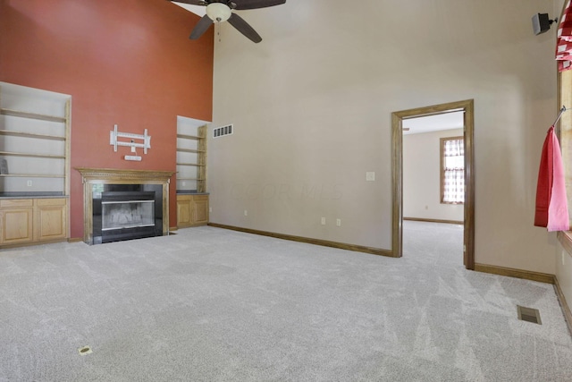 unfurnished living room with ceiling fan, built in features, light carpet, and a high ceiling