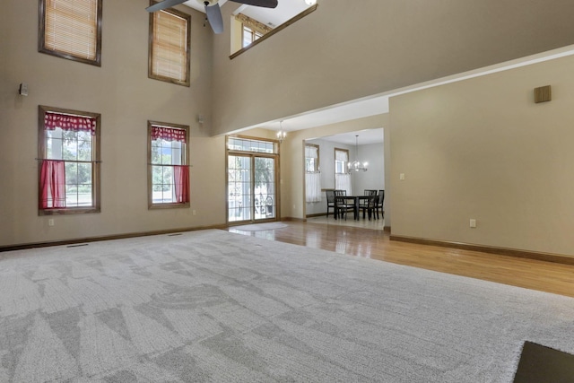 unfurnished living room with ceiling fan with notable chandelier, light hardwood / wood-style floors, and a towering ceiling