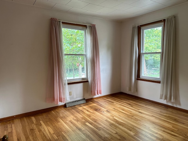 empty room with light hardwood / wood-style floors, a wealth of natural light, and a baseboard heating unit