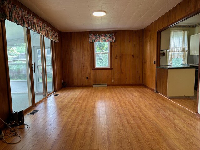 empty room featuring a baseboard heating unit, light hardwood / wood-style flooring, and wooden walls