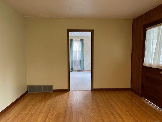 spare room with light hardwood / wood-style floors, a wealth of natural light, and wood walls