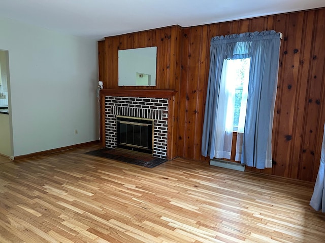 unfurnished living room with wooden walls, light hardwood / wood-style floors, and a brick fireplace