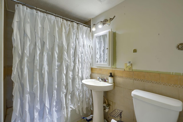 bathroom with a textured ceiling, toilet, and tile walls