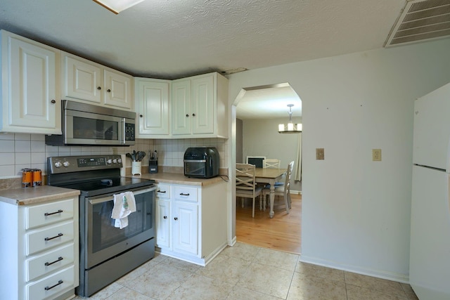 kitchen with appliances with stainless steel finishes, tasteful backsplash, a textured ceiling, white cabinetry, and light tile patterned flooring