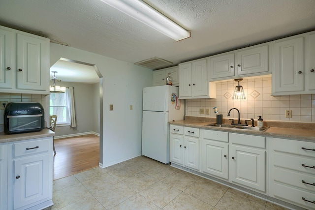 kitchen with backsplash, white refrigerator, sink, light tile patterned flooring, and white cabinetry