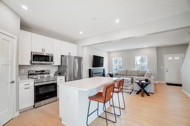 kitchen with white cabinets, a center island, light wood-type flooring, and appliances with stainless steel finishes