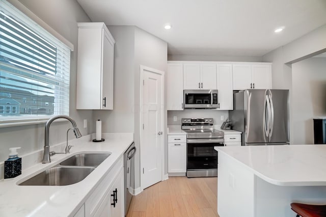 kitchen featuring white cabinets, sink, light stone countertops, light wood-type flooring, and stainless steel appliances