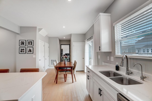 kitchen featuring light stone countertops, stainless steel dishwasher, sink, light hardwood / wood-style flooring, and white cabinetry