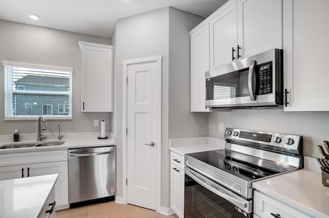 kitchen with white cabinets, sink, stainless steel appliances, and light hardwood / wood-style flooring