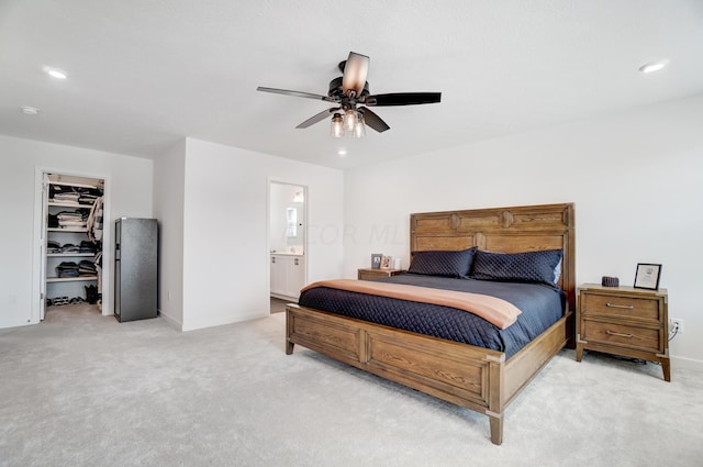 bedroom with a walk in closet, ensuite bathroom, light colored carpet, ceiling fan, and a closet