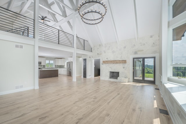 unfurnished living room with an inviting chandelier, high vaulted ceiling, beamed ceiling, a fireplace, and light wood-type flooring