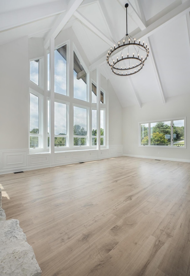 unfurnished living room featuring beamed ceiling, light hardwood / wood-style flooring, high vaulted ceiling, and an inviting chandelier