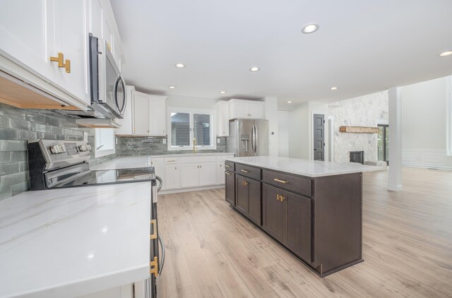 kitchen featuring appliances with stainless steel finishes, light wood-type flooring, a kitchen island, white cabinetry, and a stone fireplace