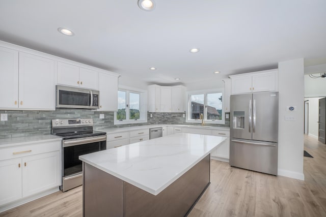 kitchen with white cabinets, light hardwood / wood-style flooring, light stone countertops, a kitchen island, and stainless steel appliances