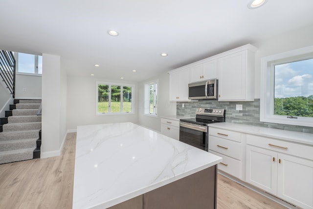 kitchen featuring light wood-type flooring, stainless steel appliances, white cabinetry, and light stone counters