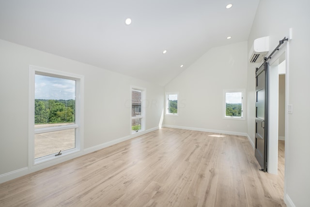 unfurnished living room featuring plenty of natural light, a barn door, a wall mounted AC, and light hardwood / wood-style flooring