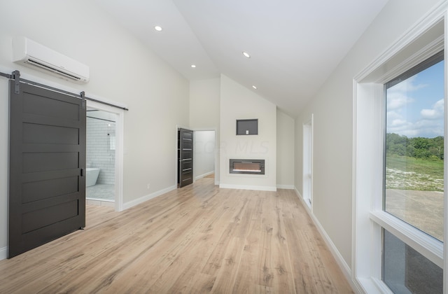 unfurnished living room with a barn door, high vaulted ceiling, light hardwood / wood-style flooring, and a wall mounted AC