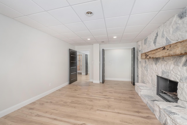 unfurnished living room featuring light wood-type flooring, a stone fireplace, and a drop ceiling