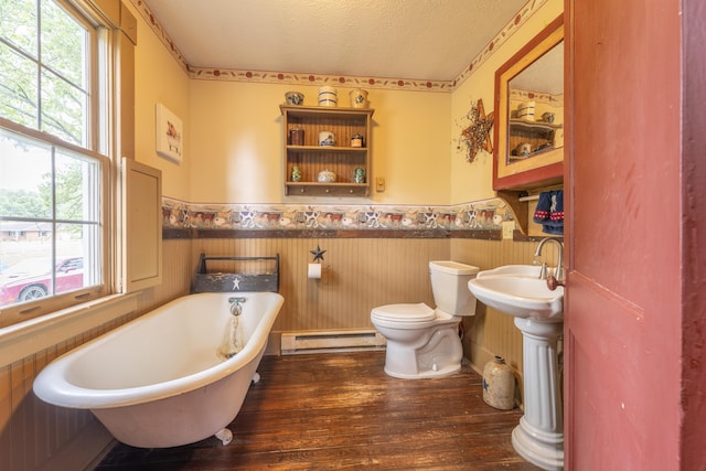 bathroom with a baseboard heating unit, a washtub, toilet, a textured ceiling, and wood-type flooring