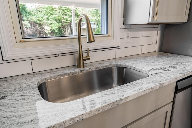 details with backsplash, light stone counters, sink, and dishwasher