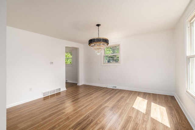 unfurnished dining area with a chandelier, a healthy amount of sunlight, and wood-type flooring