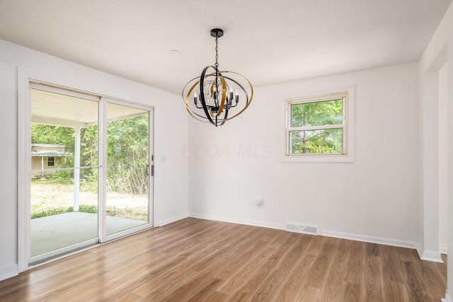 spare room with a notable chandelier, a healthy amount of sunlight, and wood-type flooring