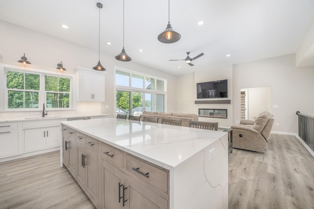 kitchen featuring white cabinets, sink, light stone countertops, light hardwood / wood-style floors, and a kitchen island