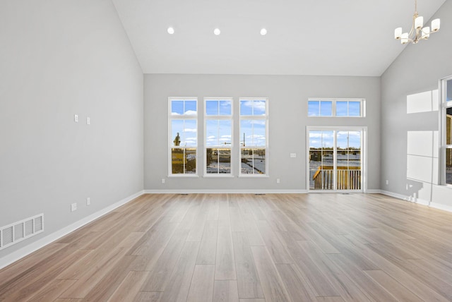 unfurnished living room featuring an inviting chandelier, high vaulted ceiling, and light hardwood / wood-style flooring