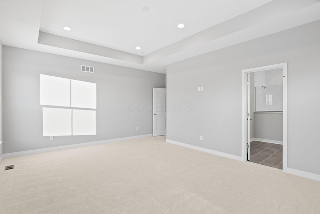 unfurnished bedroom featuring ensuite bath, a tray ceiling, and light carpet