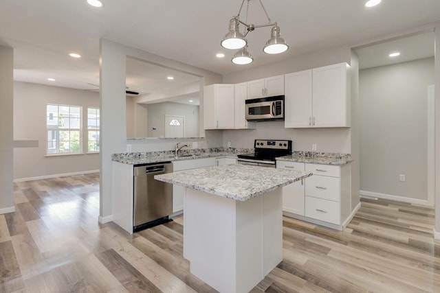 kitchen featuring white cabinetry, a center island, stainless steel appliances, light hardwood / wood-style flooring, and ceiling fan with notable chandelier