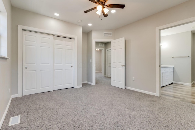 unfurnished bedroom featuring a closet, light colored carpet, ceiling fan, and ensuite bathroom