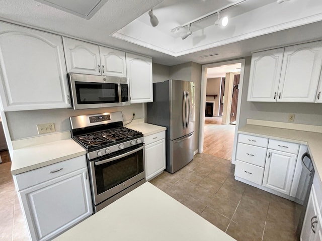 kitchen with rail lighting, a textured ceiling, stainless steel appliances, light tile patterned floors, and white cabinetry