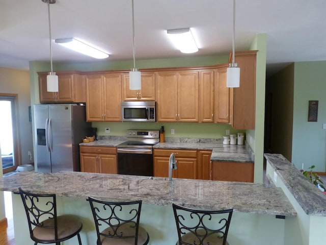 kitchen with light stone countertops, stainless steel appliances, hanging light fixtures, and light hardwood / wood-style flooring