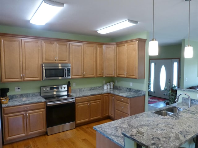 kitchen with sink, light stone counters, light hardwood / wood-style flooring, decorative light fixtures, and appliances with stainless steel finishes