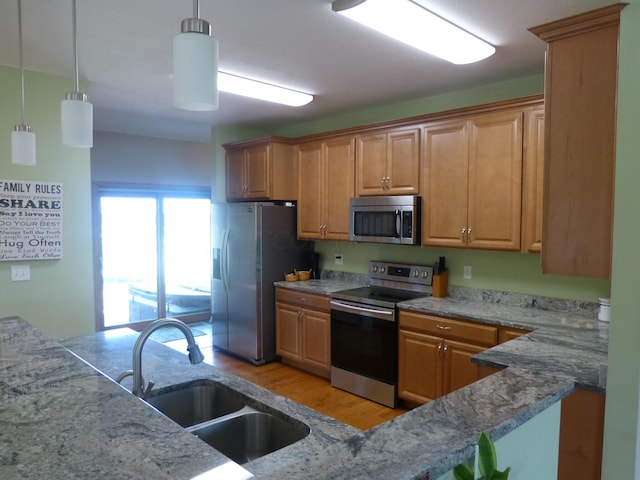 kitchen with pendant lighting, sink, light wood-type flooring, light stone counters, and stainless steel appliances