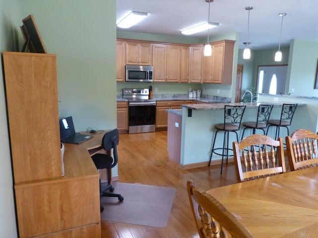 kitchen with light brown cabinets, stainless steel appliances, light hardwood / wood-style flooring, and hanging light fixtures