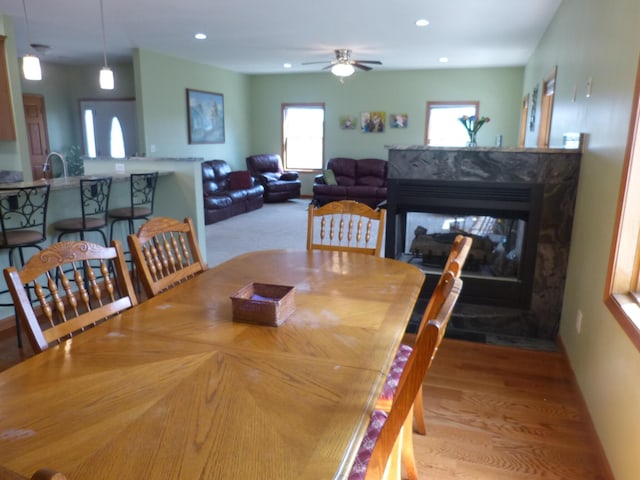 dining area featuring a multi sided fireplace, ceiling fan, and light hardwood / wood-style flooring