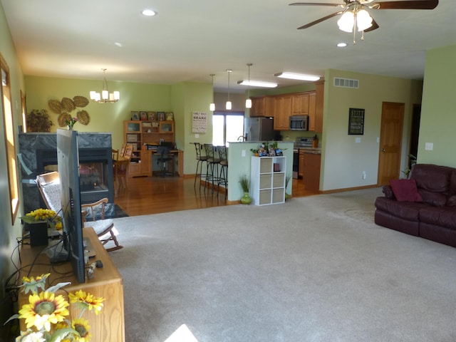 carpeted living room with ceiling fan with notable chandelier and a high end fireplace