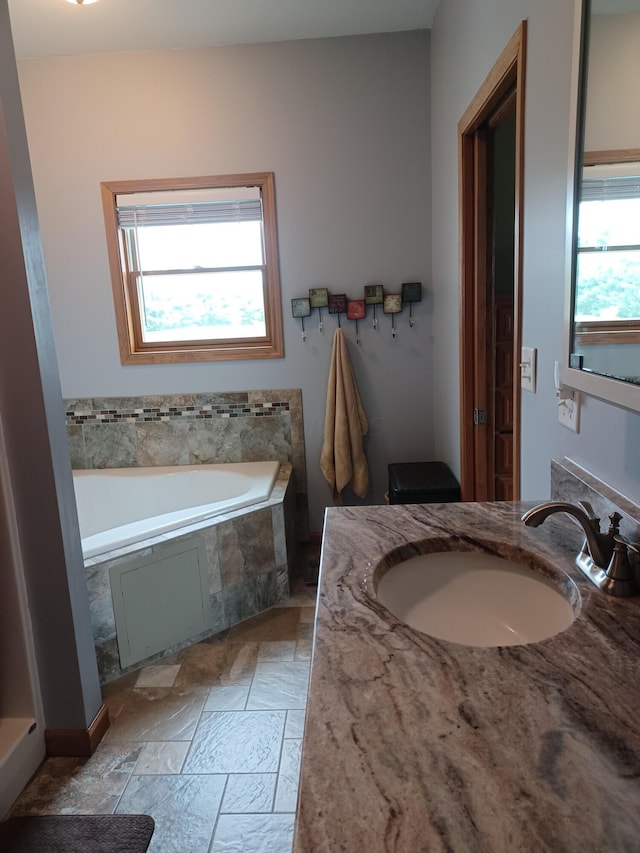 bathroom featuring vanity, a healthy amount of sunlight, and tiled tub