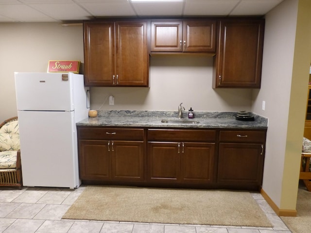 kitchen featuring a drop ceiling, dark brown cabinets, sink, light tile patterned floors, and white refrigerator