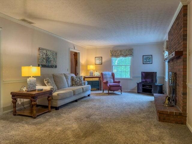 living room with a fireplace, carpet, a textured ceiling, and ornamental molding