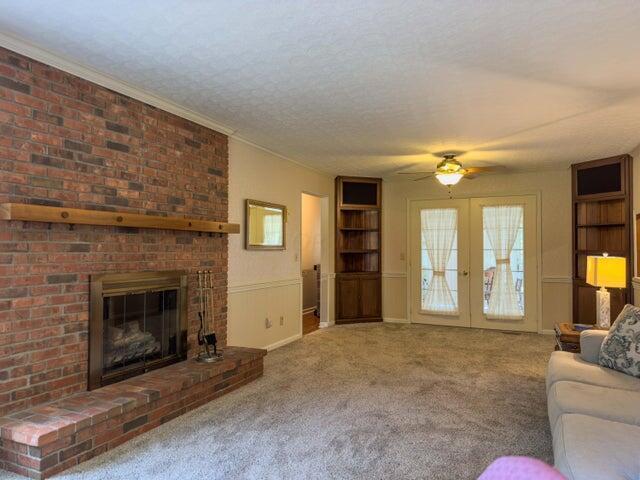 carpeted living room with french doors, ornamental molding, a textured ceiling, ceiling fan, and a fireplace