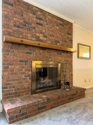 details with carpet, a brick fireplace, and ornamental molding