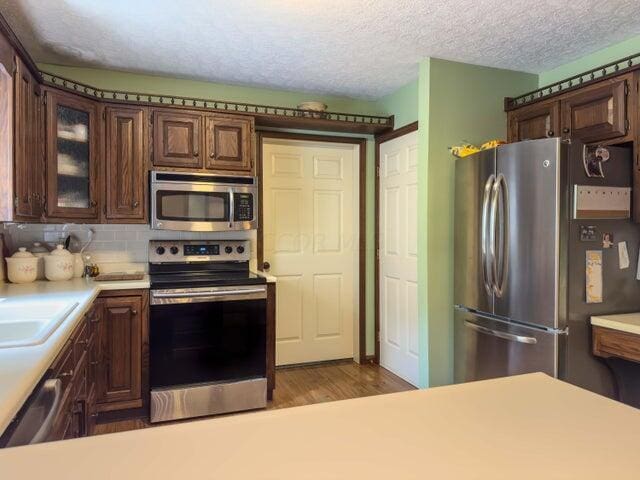 kitchen with dark brown cabinetry, stainless steel appliances, tasteful backsplash, light hardwood / wood-style flooring, and a textured ceiling