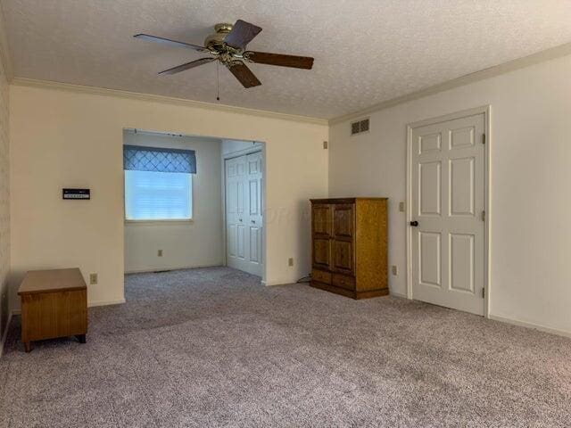 spare room with a textured ceiling, light colored carpet, ceiling fan, and crown molding